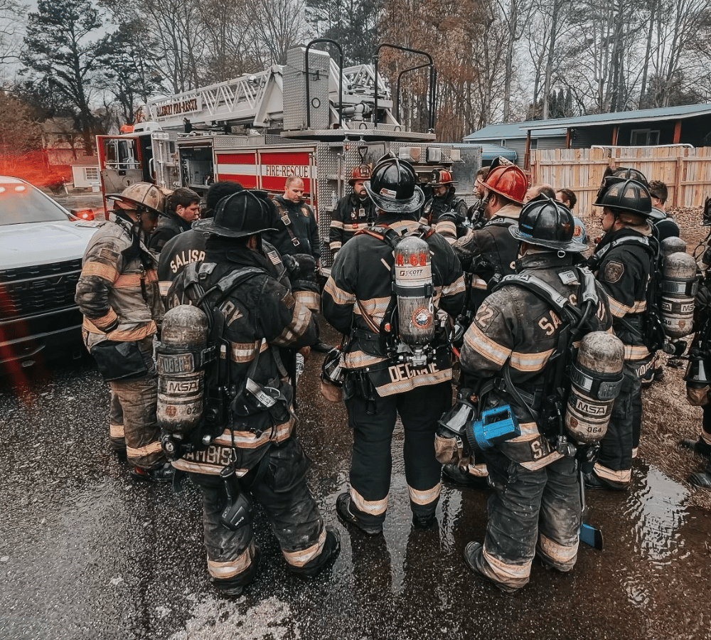 Combat Ready Firefighters gathered together in uniform around firetruck